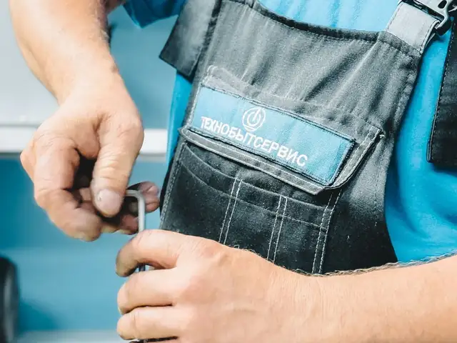 A plumber's hands turning a wrench on indoor pipes.